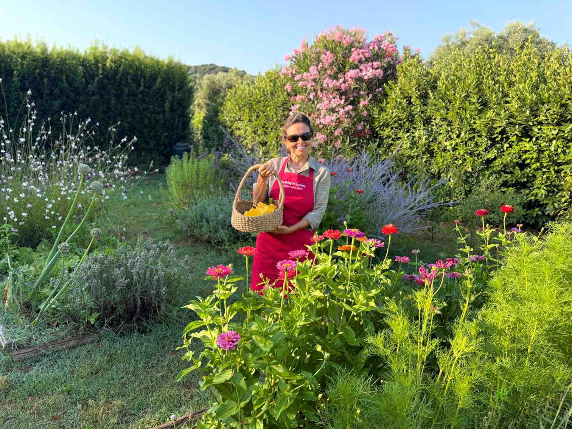 Chicca in Her Tuscan Garden Chicca standing in a lush Tuscan garden full of flowers and herbs, holding a basket of fresh vegetables