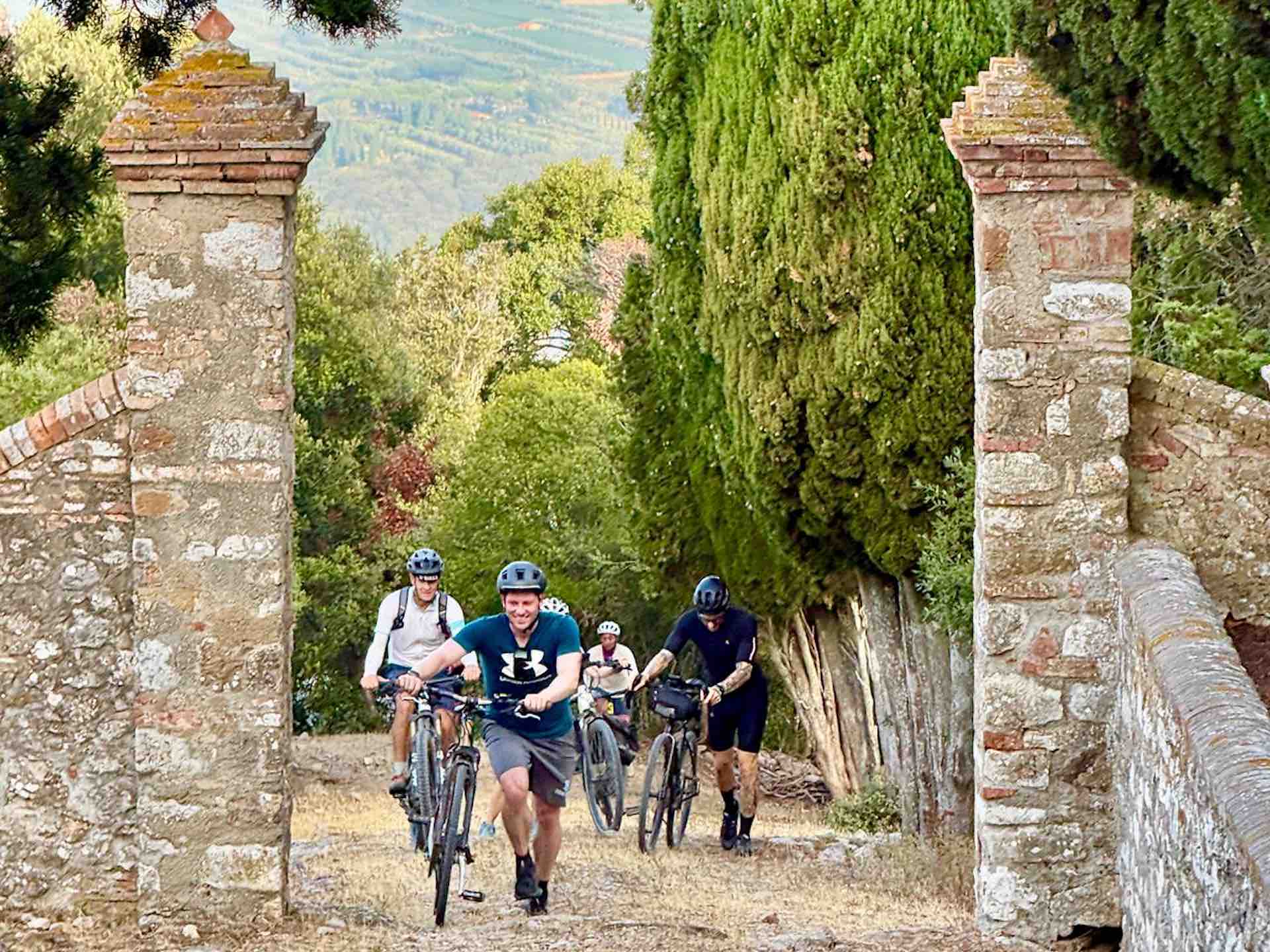 Cycling Through the Castiglioncello di Bolgheri Gate Group of cyclists riding bicycles through an old stone gate on the private road to Castiglioncello di Bolgheri